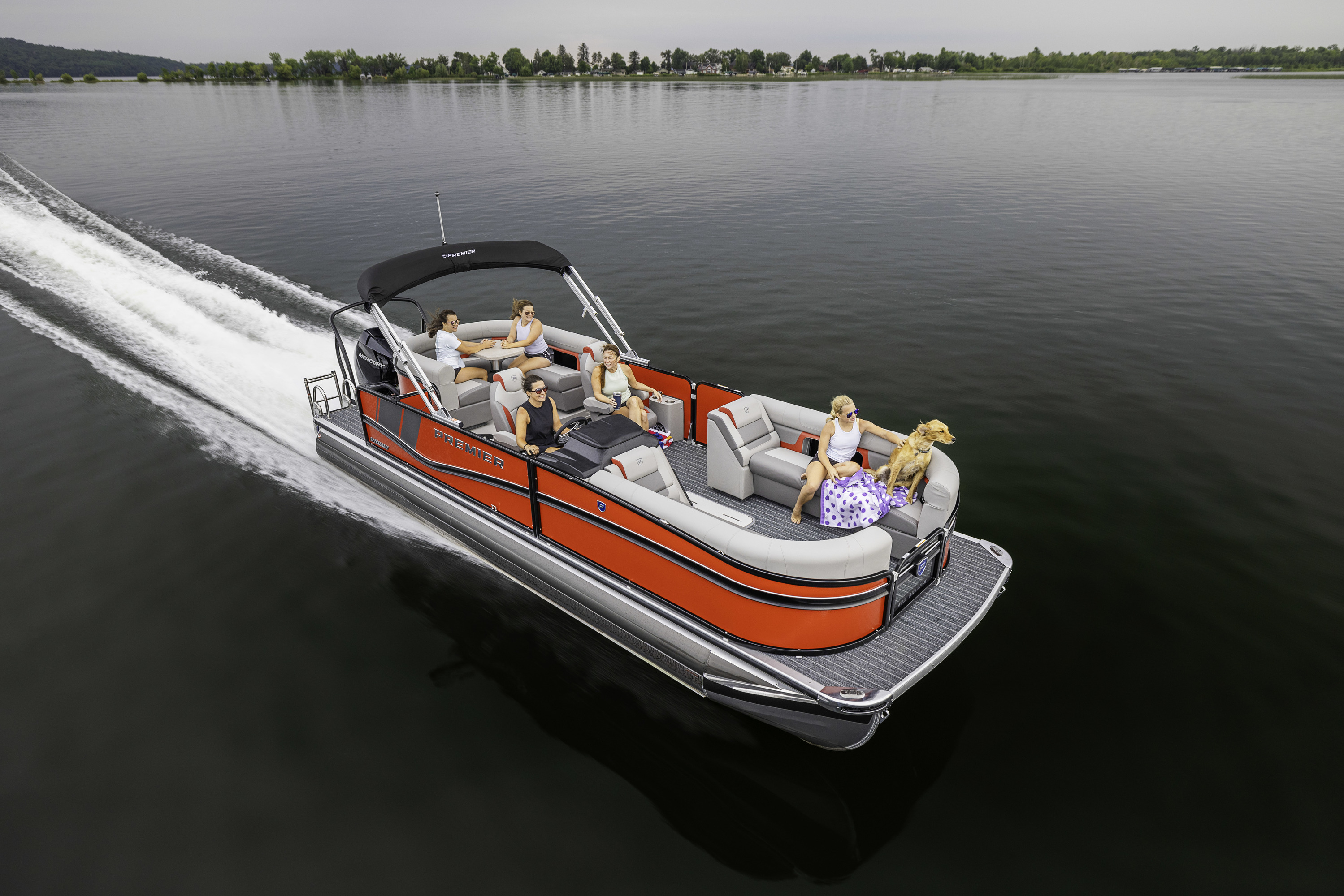 A group of people ride in a speeding Premier® Sunsation pontoon boat on the water during a sunny day